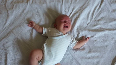 Baby is crying lying on the big bed. The child is dressed in body and diapers Stock Footage