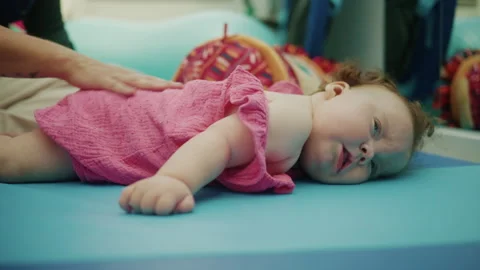 Baby with Down syndrome lying on a mat, receiving early intervention therapy. 스톡 동영상 343377328