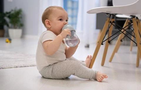 A baby is drinking from a bottle while sitting on the floor Stock Photos