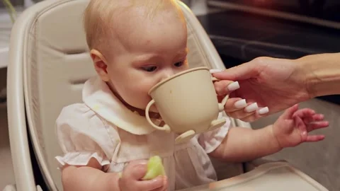Baby drinking from a cup while sitting in a high chair with a parent's help Vidéo 342503915
