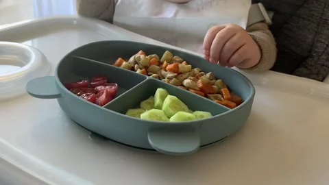 Baby eating first solid food in a silicone plate on the table of high chair Stock Footage 304735739