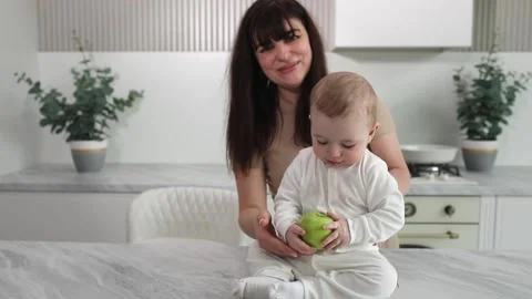 Baby eats apple with mom in kitchen Stock Footage 237916888