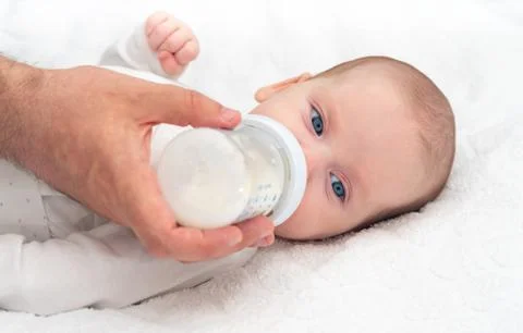 Baby eats formula from a bottle supported by his father Stock Photos