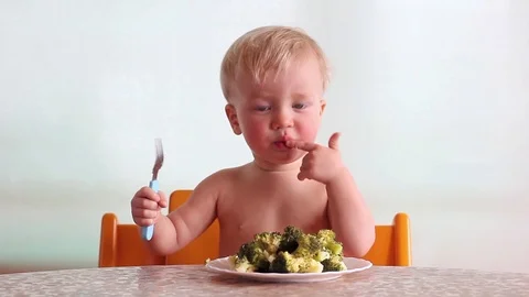 Baby eats with pleasure broccoli by fork and hand, licks finger, happy kid Видео 88088435