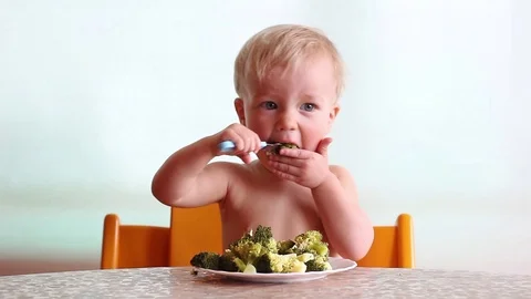 Baby eats with pleasure steamed broccoli by fork, happy kid, white background Stockbeeldmateriaal 88087398