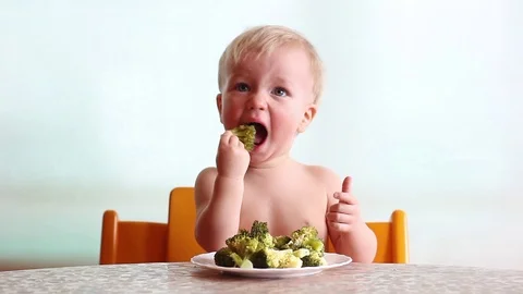 Baby eats with pleasure steamed broccoli by hand, happy kid, white background Video stock 88087847