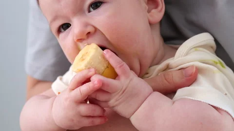 A baby eats solid food in the mother's arms. The principle of "baby-led feeding" Stock-Footage 329864351