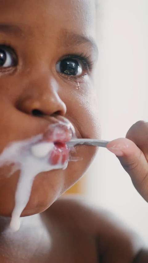 Baby eats yogurt sitting in a high chair Stock Footage 246772292