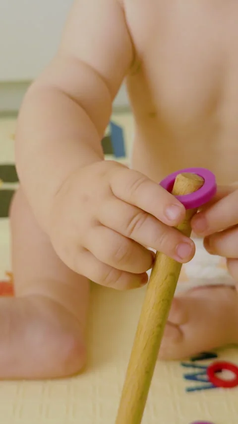 Baby engages in playful learning by stacking colorful rings on a wooden post Stock Footage 331806172