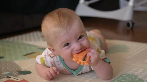 Baby enjoying tummy time while biting a toy shows active learning, play, and Stock Footage 316038333