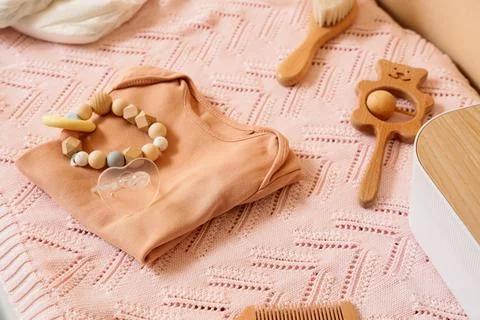 Baby essentials flat lay with a peach bodysuit, wooden teether, pacifier, and Stock Photos