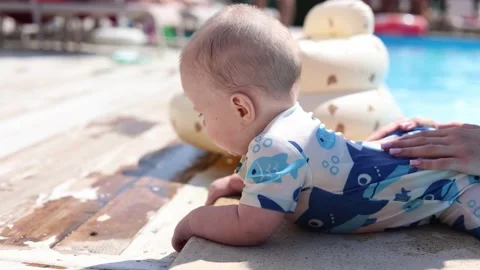 Baby explores a sunlit poolside while an adult offers steady support near the Stock Footage 347687395