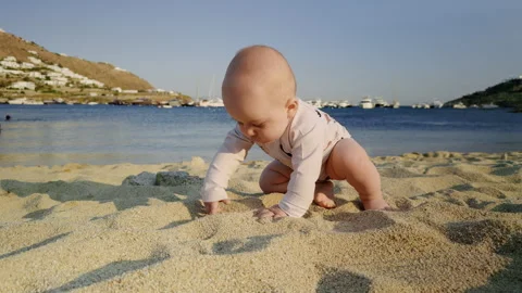 Baby exploring sandy beach, playing with grains of sand, surrounded by calm sea Stock Footage 317328605