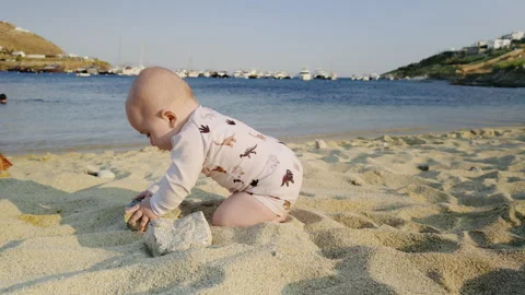Baby exploring sandy beach, playing with small rocks, surrounded by gentle waves Stock Footage 318217154