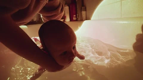 A baby float in a bath, the warm water glowing around them. Gentle hands guide 動画素材 264497063