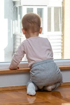 Baby gazes longingly through window, eager for an outdoor adventure. Concept of Stock Photos