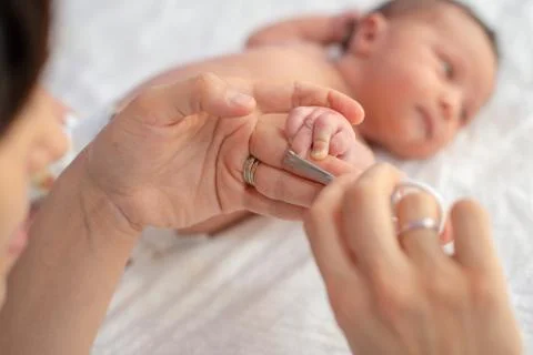 Baby getting fingernails cut while sleeping by his mother with scissors. Nurs Stock Photos