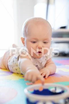 Baby girl with blue eyes playing on mat at floor Stock Photos
