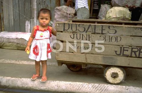 Baby girl child kid stands next junk cart gaze Stock Photos