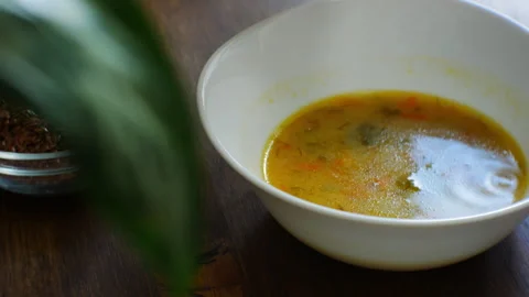 Baby girl eats vegetable soup reluctantly. Kitchen table made of solid wood Stock Footage 280564341