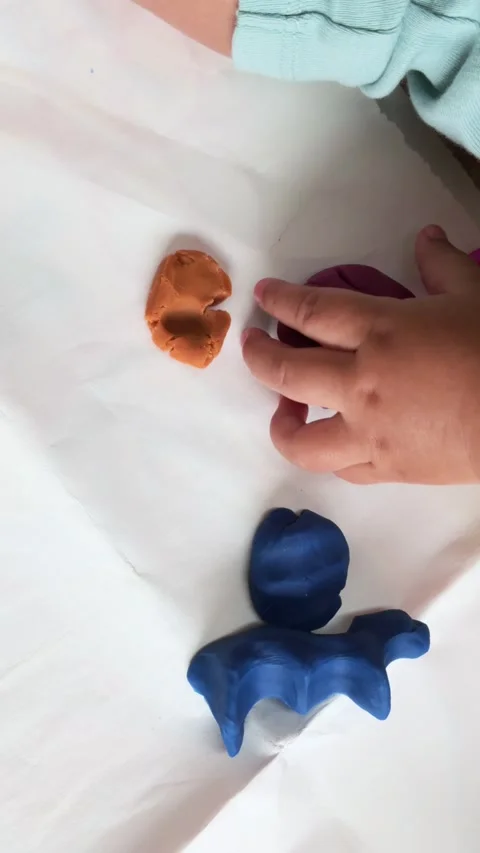 Baby hands reaching on the second attempt for colorful playdough on white paper Stock Footage 312967194