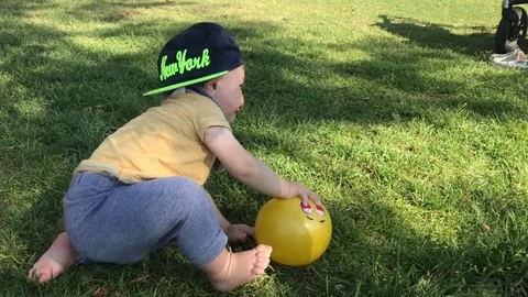 Baby in hat plays with ball on grass in park. Sunny day. Stock Footage
