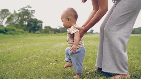 Baby learning to walk first step with mother on green grass, happy family baby Stock Footage 202080715
