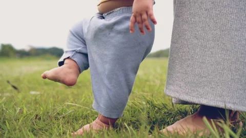 Baby learning to walk first step with mother on green grass, happy family baby Stock Footage 202858056