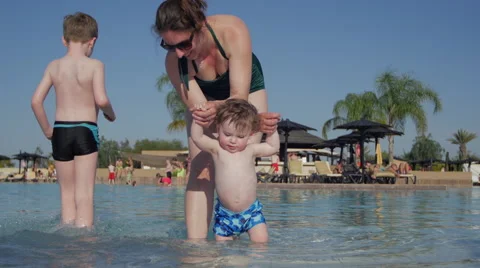 Baby learning to walk in pool by hand on holiday in pool Stock Footage 49703206