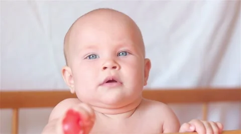 Baby looking into the camera, standing in bed and holding a toy Stock Footage 67660718