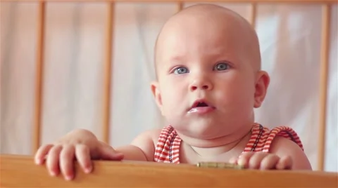 Baby looking into the camera, standing in bed and holding a toy Stock Footage 67700904