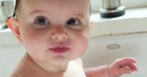 A baby looking into the camera while getting a bath in a kitchen sink. Stock Footage 130355755