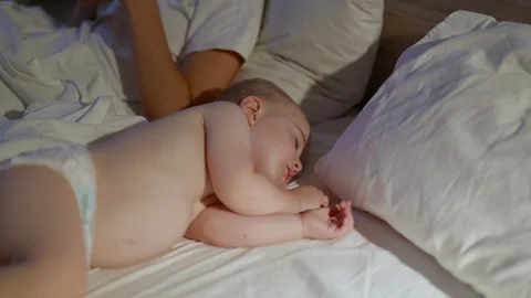 Baby lying on bed with white sheets and pillows, peacefully sleeping beside an Stock Footage 341898827