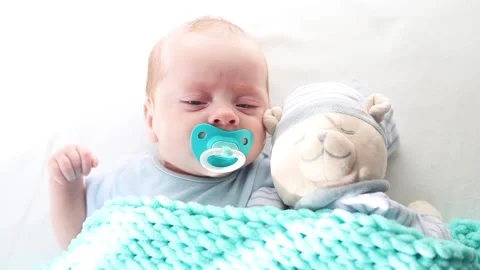 The baby is lying in a crib with a teddy bear . The baby is 0-3 months old. A Stock Footage 194092003