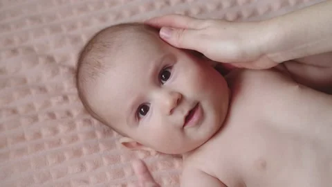 Baby lying on its back on the bed. Mother touches her baby's head with her hand Stock Footage 150118017