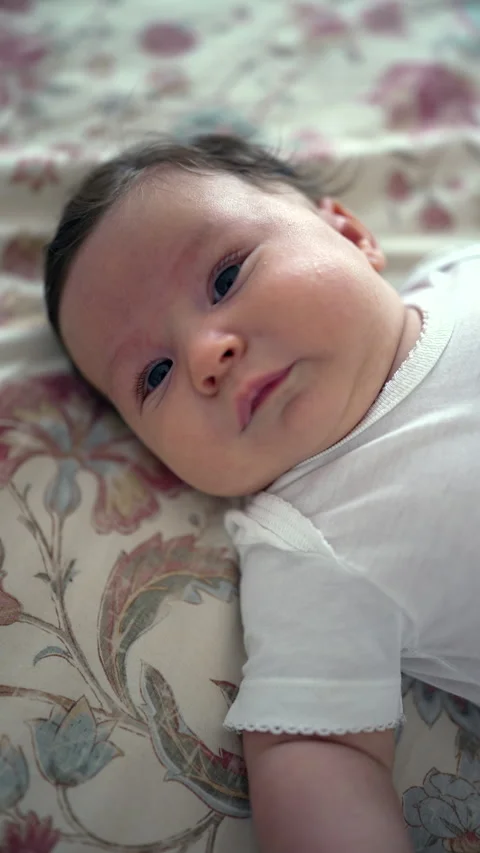 Baby lying on a patterned blanket, showing a subtle smile. close-up capture.. Stock Footage 285876170