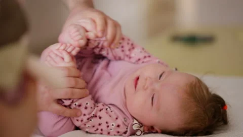 A baby is lying on a soft changing surface while an adult gently holds both of Stock Footage 335535713