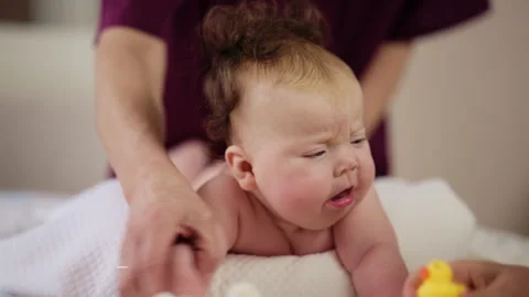 Baby lying on their tummy while an adult massages them and performs mobility Video stock 329401617