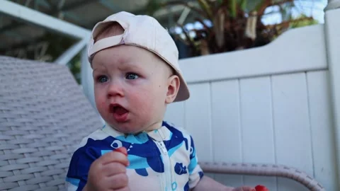 Baby makes expressive faces while seated outdoors in a blue patterned shirt and Stock Footage 347686528