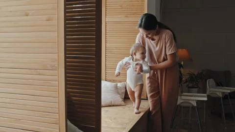 Baby Making First Steps On Window Sill, Supported By Mom Vídeos de archivo 241003521