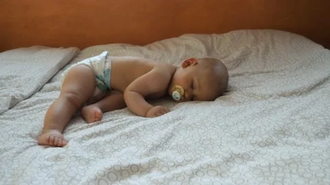 A baby napping on a big bed with his pacifier, in France Stock Footage 212085309