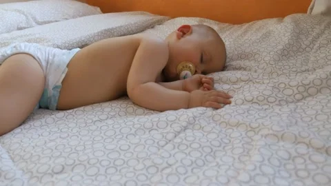 A baby napping on a big bed with his pacifier, in France Stock Footage 212131276
