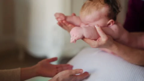 Baby placed on a stability ball while adults support the infant's body Stock Footage 329400120