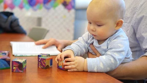 Baby playing with cubes while sitting on his father's arms. Close portrait, the Stock Footage 103359781