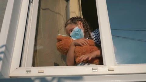 The baby is playing with a Teddy bear in a protective mask and looks out the Stock Footage 138916573