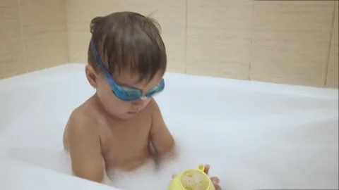 A baby plays with bubbles while taking a bath. Glasses Stock Footage 77260486