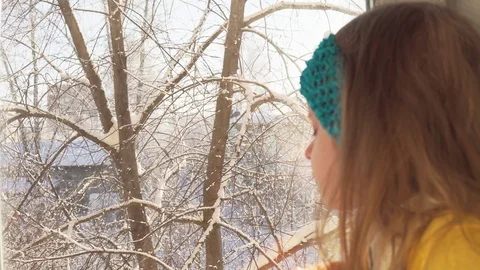 Baby plays sitting on the windowsill on the background of snow-covered trees. Stock Footage 108119494