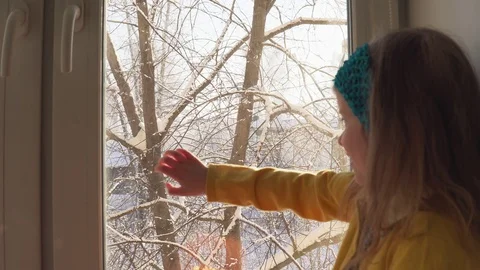 Baby plays sitting on the windowsill on the background of snow-covered trees. Stock Footage 108119678
