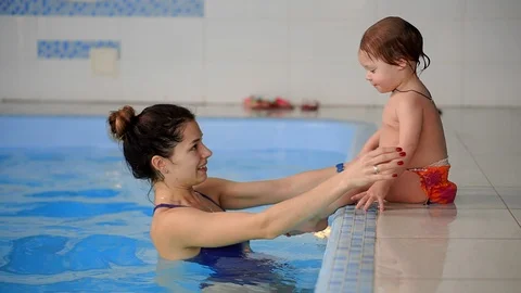 Baby in the pool jumping from the side into the water and swims to his mother in Stock Footage 101776582