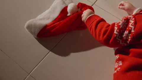 Baby pulls off his Santa hat with tiny hands as a Christmas decoration rolls Stock Footage 295357313